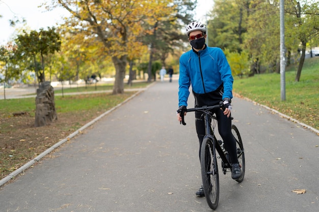 自転車道の公園で、眼鏡と保護マスクを着用したアスリートが自転車に座っています。検疫されたスポーツとアウトドアレクリエーション。