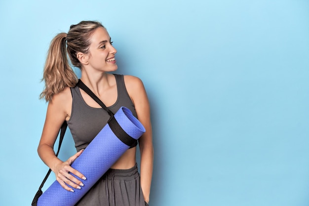 Athlete holding an exercise mat in blue studio