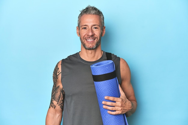 Athlete holding a fitness mat on blue studio background