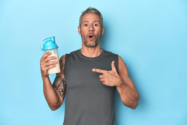 Athlete holding protein shake on blue backdrop pointing to the side