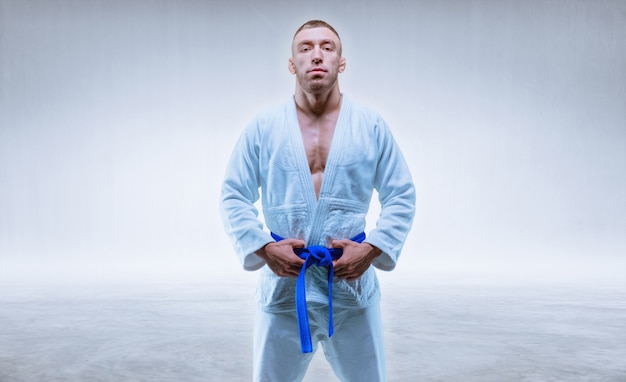 Фото Спортсмен в кимоно с синим поясом стоит на светлом фоне. понятие карате и дзюдо. смешанная техника