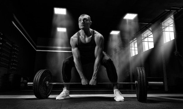 Athlete is standing on his knee and near the bar and is preparing to make a deadlift. Mixed media