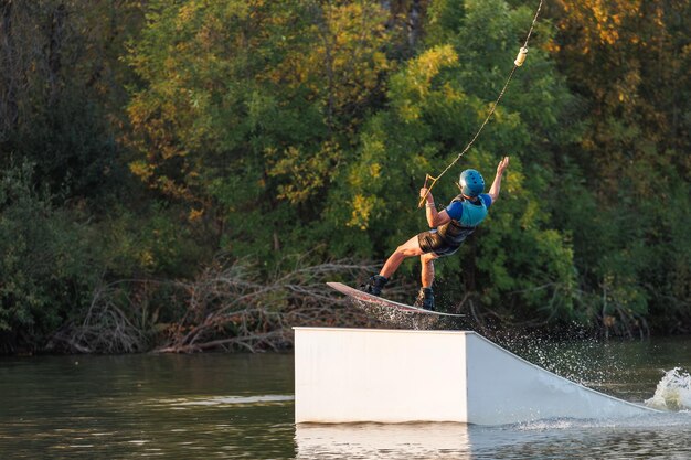 An athlete jumps from a springboard Wakeboard park at sunset A man performs a trick on a board