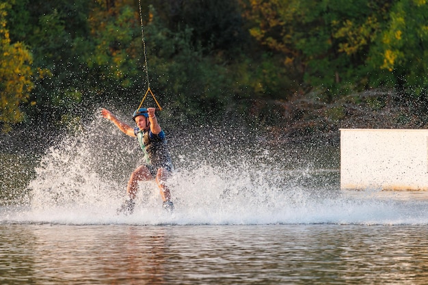 Спортсмен прыгает через воду Вейкборд-парка на закате Райдер выполняет трюк на доске