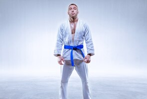 Athlete in a kimono with a blue belt stands on a light background. the concept of karate and judo. mixed media