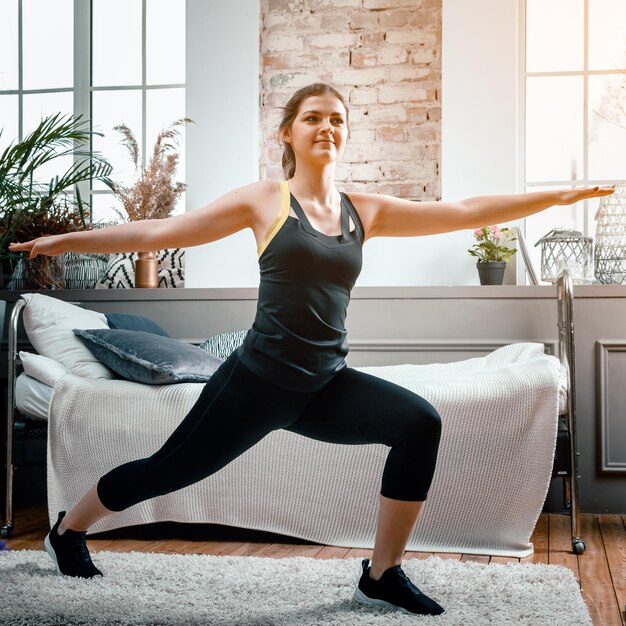 The athlete lunges in the bedroom in the background there is a bed a vase a carpet