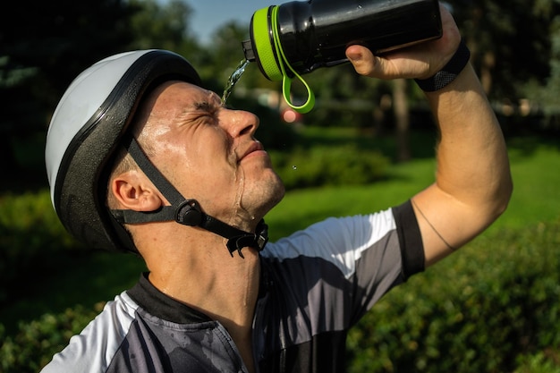 An athlete a man in a helmet a cyclist drinks water quenches his thirst