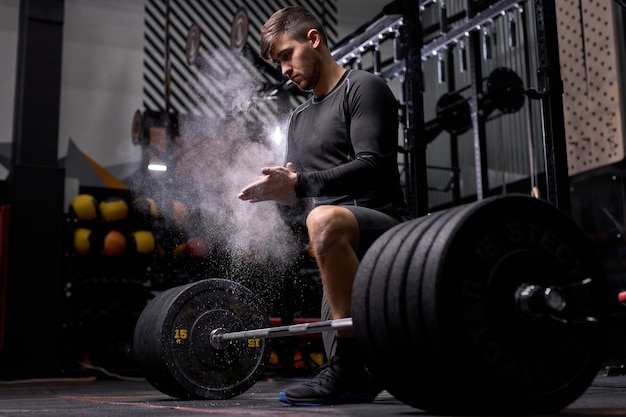 운동 선수 남자는 크로스 핏 훈련을 준비하고 있습니다. Cnfident powerlifter는 무거운 무게를 올리기 위해 활석을 사용합니다. 현대적인 체육관, 피트니스 센터에서