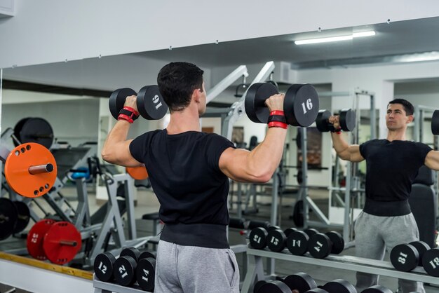 Athlete man lifting dumbbell in gym, back view