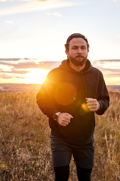 フィールドの山に沿って日没または日の出で走る、朝のジョギングをする運動選手の男