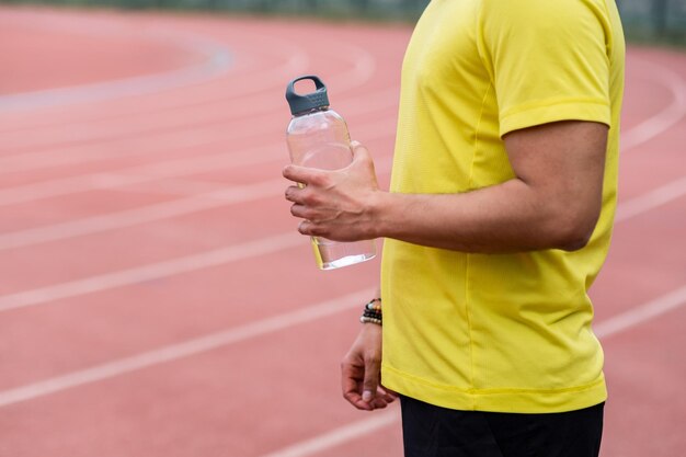 Athlete man takes a moment to catch his breath on the running track holding refreshing water bottle