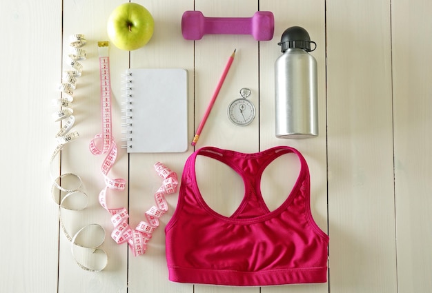 Athlete's set with female clothing equipment apple bottle of water and notebook on white wooden background