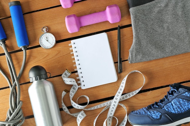 Photo athlete's set with female clothing equipment bottle of water and notebook on wooden background