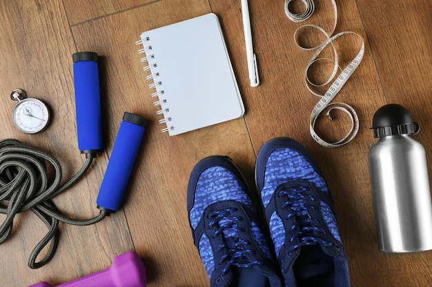 Athlete's set with female sneakers bottle of water equipment and notebook on wooden background
