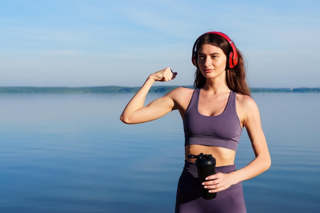 Спортсменка показывает свои бицепсы после тренировки на свежем воздухе Тренировка в море