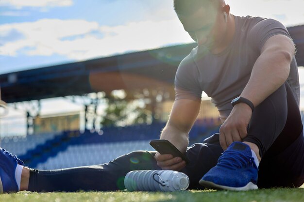 Athlete sits on the lawn after training texting messages in the chat on phone