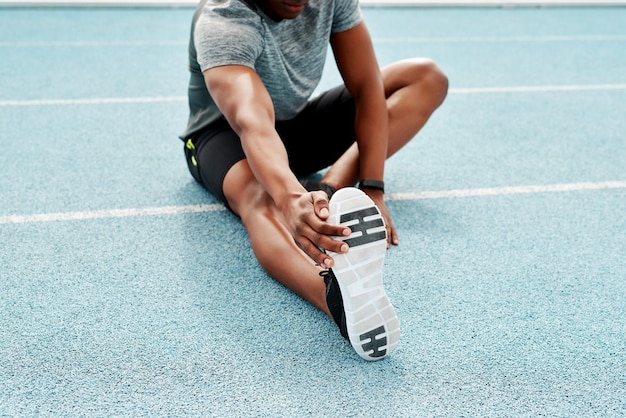 Photo athlete sitting and track for stretching legs to start training exercise or running for fitness outdoor man runner and warm up for muscle body and wellness at stadium for race contest or sports