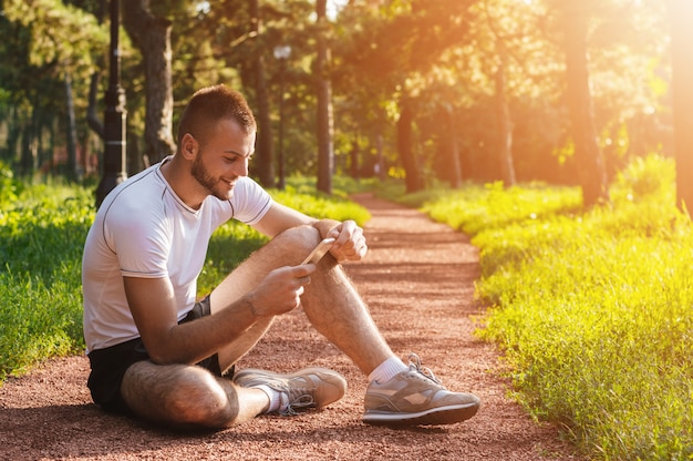 Athlete or sports trainer checking his mobile phone in the park