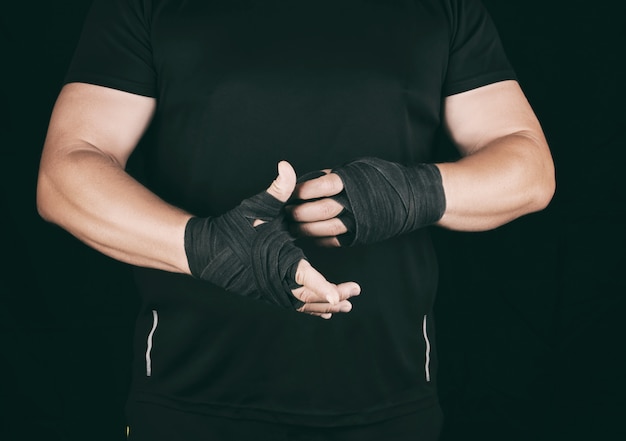 Athlete stand in black clothes and wrap his hands in textile elastic bandage