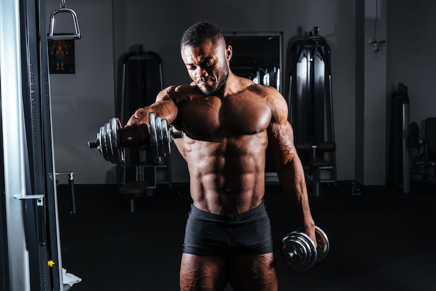 Athlete with dumbbells in hands in the gym