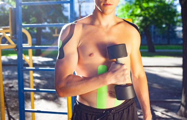 Athlete with kinesiological taping posing at sports ground.