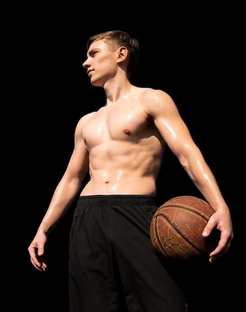 Спортсмен с голым торсом и баскетбольным мячом, изолированные на черном фоне