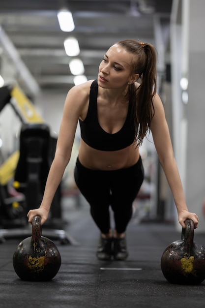 Athlete woman doing push ups on two kettlebells