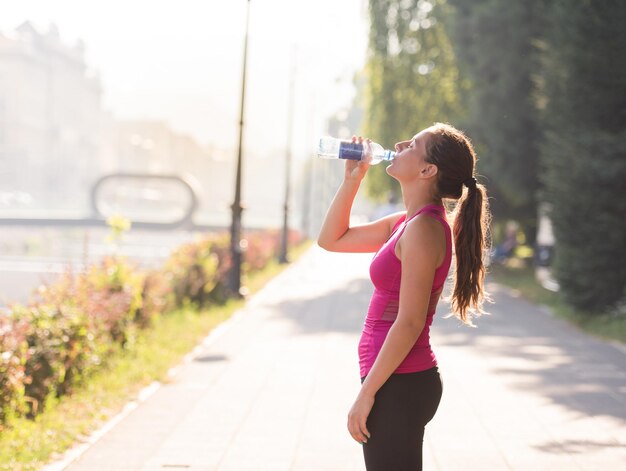 Athlete woman drinking water from a bottle after jogging in the city on a sunny day