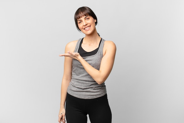 Athlete woman smiling cheerfully, feeling happy and showing a concept in copy space with palm of hand