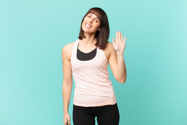 Athlete woman smiling happily and cheerfully, waving hand, welcoming and greeting you, or saying goodbye