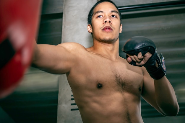 フィットネスジムでサンドバッグトレーニングアスリートアジア男ボクサー。