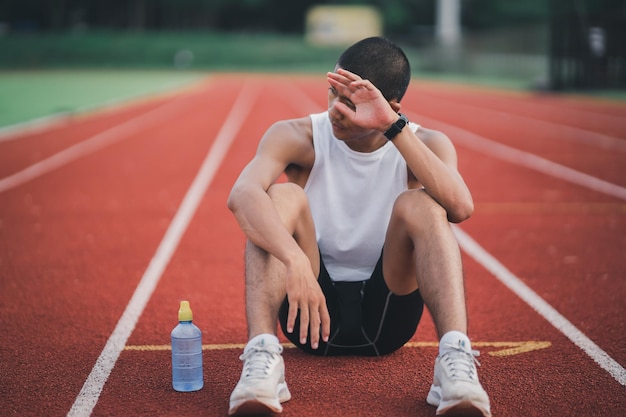 Спортсмены-бегуны отдыхают в бутылке с водой, уставшие и испытывающие жажду, тренирующиеся на беговой дорожке на стадионе. Беговые тренировки с питьевой водой.