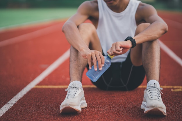 Athletes runner sport man resting holding bottle water tired\
and thirsty practicing on a running track at a stadium running\
workout drinking water sport man run concept