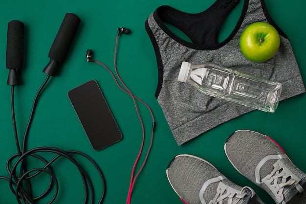 Athletes set with female clothing and bottle of water on green background