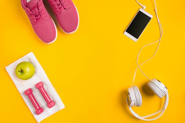 Athletes set with female clothing dumbbells and bottle of water on yellow background