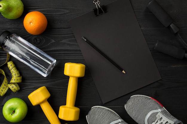 Athletes set with female clothing sneakers and bottle of water on dark background