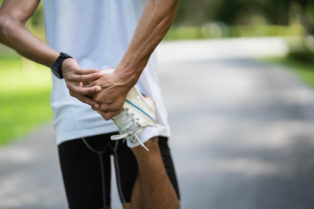 Athletes sport man runner wearing white sportswear to stretching foot and legs and warm up before practicing on a running track at a stadium park Runner sport concept