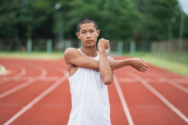 Athletes sport man runner wearing white sportswear to stretching and warm up before practicing on a running track at a stadium Runner sport concept