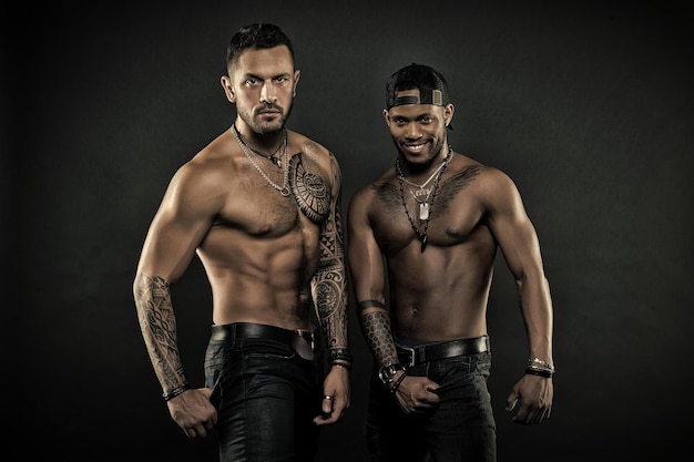 Athletes with tattooed arms and chests Men with six pack promoting healthy lifestyle fitness concept Bodybuilders with sexy bodies African and Hispanic men posing isolated on black background