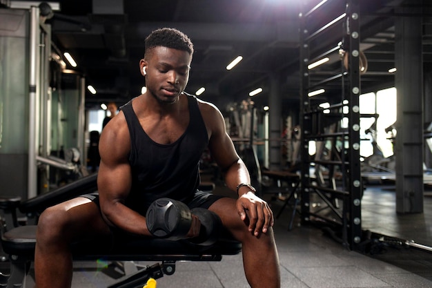 Photo athletic african american man trains in dark gym athletic guy lifts heavy dumbbells in fitness club