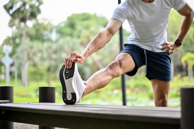 Athletic Asian man is stretching his leg on a bench warming up or cooling down cropped