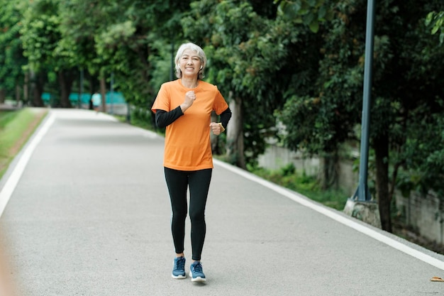 Donna senior asiatica atletica che esegue jogging all'aperto nel parco