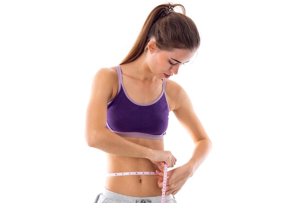 Athletic athletic woman in purple sports top using centimeter on white background in studio