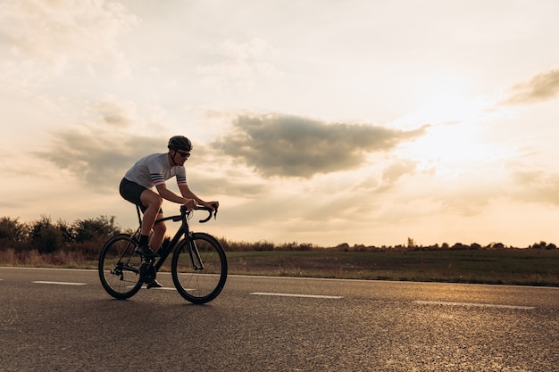 Athletic bearded man in sport clothing and protective helmet riding bike on asphalt road