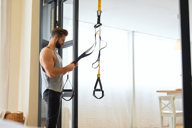 Athletic bearded man in sportswear preparing fitness equipment for home workout