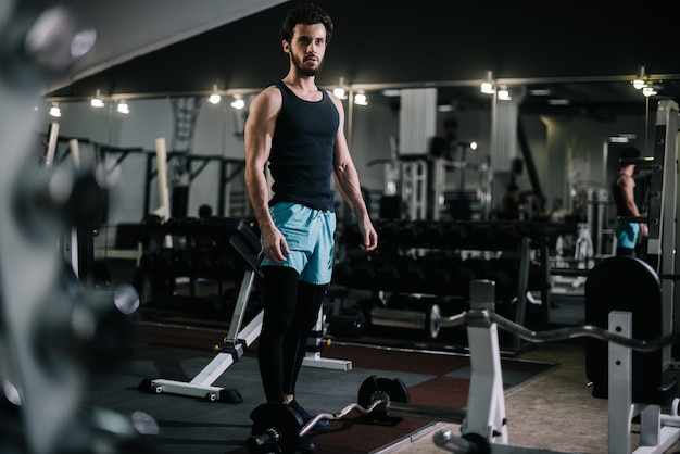 Athletic bearded young man with muscular wiry body wearing sportswear posing in modern dark gym