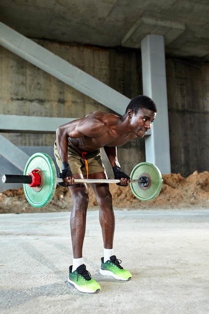 Athletic black young man lifting a heavyweight barbell in outdoor gym under the bridge Healthy lifestyle concept