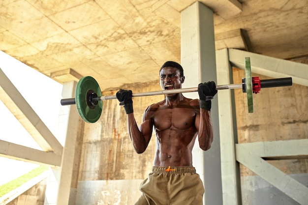 Athletic black young man lifting a heavyweight barbell in outdoor gym under the bridge Healthy lifestyle concept