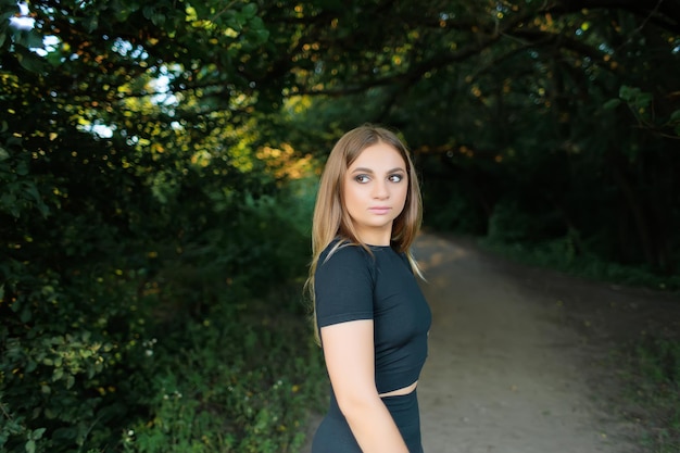 Athletic blonde girl stands on the path in the park and looks away