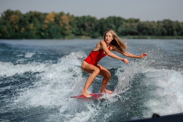 Donna bionda atletica che pratica il surfing a bordo giù l'acqua blu